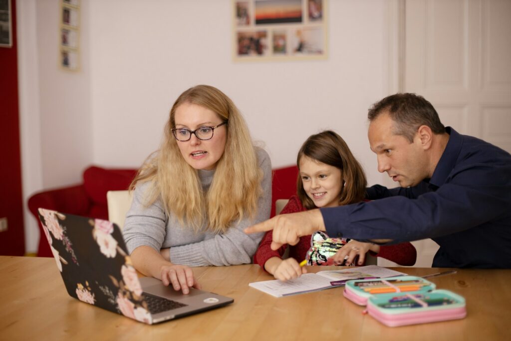 Two adults helping a child with schoolwork on a laptop