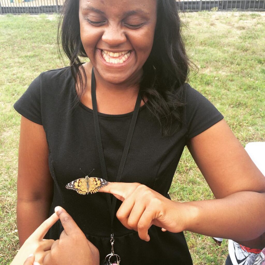 Vimbo Watson sharing a butterfly with a student during an outdoor science lesson