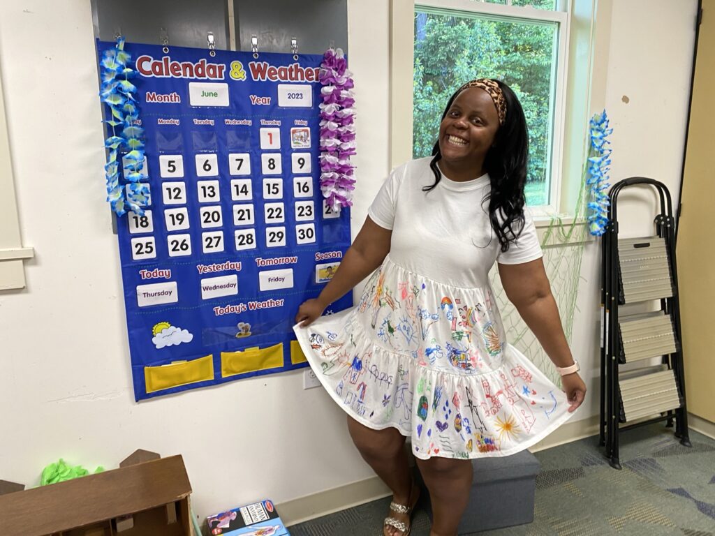 Vimbo Watson smiling in front of a classroom calendar wall
